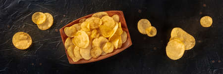 Potato chips or crisps, a salty snack, overhead flat lay panorama on a black slate backgroundの写真素材