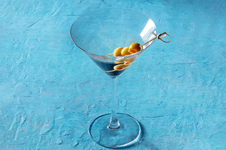 Martini, a glass with spicy olives on a toothpick, on a blue background. Alcoholic aperitif