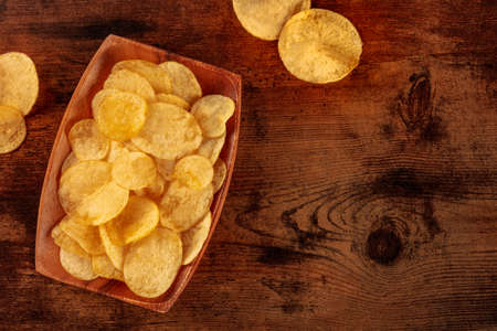 Potato chips or crisps in a bowl, shot from the top on a wooden background with a place for textの写真素材
