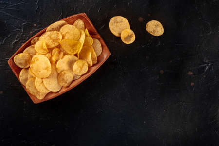 Potato chips or crisps in a bowl, overhead flat lay shot on a black slate background with copy spaceの写真素材