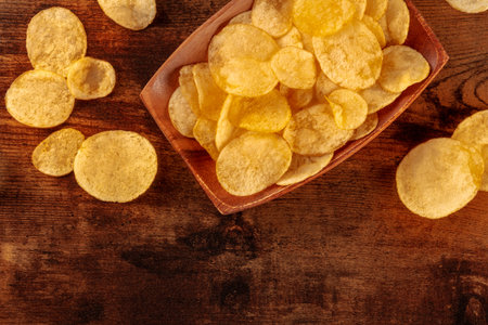 Potato chips or crisps in a bowl, shot from the top on a wooden background with a place for textの写真素材