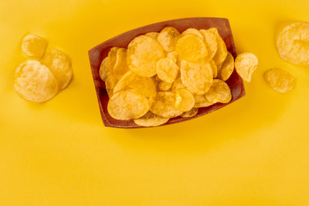 Potato chips or crisps, a salty snack in a bowl, shot from above on a yellow background with copy...