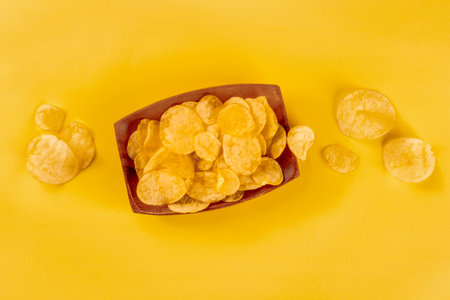 Potato chips or crisps, a salty snack in a bowl, overhead flat lay shot on a yellow background with copy spaceの写真素材