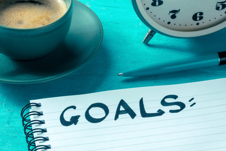 Goal setting. A notepad with the handwritten word on a desk, with a pen, an alarm clock, and a cup...