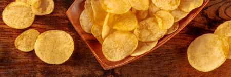 Potato chips or crisps, a salty snack on a wooden background, a panoramic header, top shot