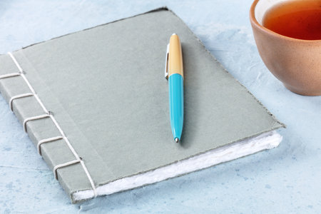 A diary. A paper journal with a pen and a cup of tea on a deskの写真素材