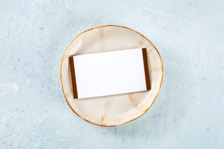 Dinner invitation. A card on a ceramic plate with a gold rim, overhead flat lay shot. Place setting