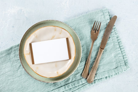 Dinner invitation. A card on a plate, with silverware and a teal textile napkin, overhead flat lay shot. Place settingの写真素材