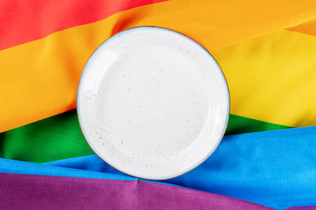 Gay food concept. A plate, overhead flat lay shot on the LGBTQ rainbow flag texture, a dinner party invitation designの写真素材
