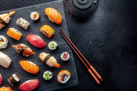 Sushi overhead flat lay shot with chopsticks, tea, and copy space. Rolls, maki, nigiri on a black background, Japanese food. Salmon, tuna, eel, shrimp and other seafoodの写真素材