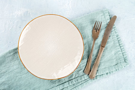 An empty white plate with a gold rim, with a fork and a knife, overhead flat lay shot, the concept of dinnerの写真素材