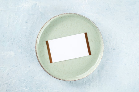Dinner invitation. A card on a green plate, overhead flat lay shot on a slate background. Place settingの写真素材