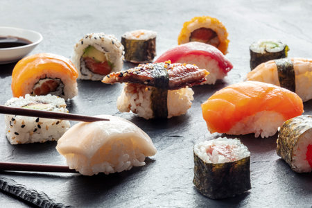 Sushi with chopsticks on a black slate background. Rolls, maki, nigiri, Japanese food. Whitefish, eel, salmon and other seafood with rice on a plate at an Asian restaurantの写真素材