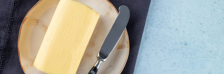 Butter panorama with copy space. A block of butter with a knife on a plate, overhead flat lay shot...