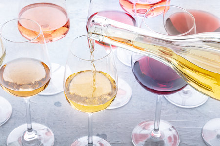 White wine pour into a glass at a tasting. Rose, red, and white wine, drinks on a table at a winery. An assortment of wines of many different colorsの写真素材