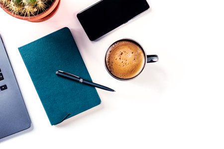 Desk, top view on a white background. Coffee, notebook, phone, plant, and laptop, overhead flat lay shot. Work layout with copy spaceの写真素材