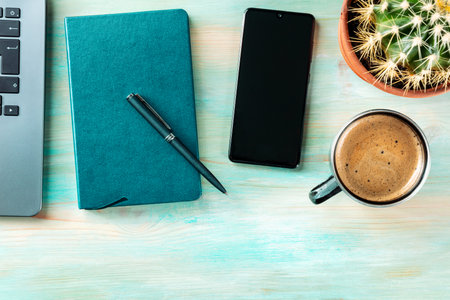 Desk, top view on a wooden blue background. Coffee, notebook, phone, plant, and laptop, overhead flat lay shot. Work layout with a place for textの写真素材