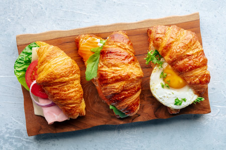 Croissant sandwich variety. Various stuffed croissants, overhead flat lay shot on a wooden board. Rolls filled with ham, salmon, egg, etcの写真素材