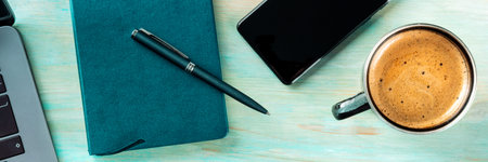 Desk, top view on a wooden blue background panorama. Coffee, notebook, phone, plant, and laptop,...