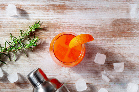 Orange cocktail and a shaker, with rosemary and ice, overhead flat lay shot on a wooden background with copy spaceの写真素材
