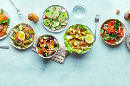 Fresh salads, overhead flat lay shot of an assortment. Variety of plates and bowls with green...
