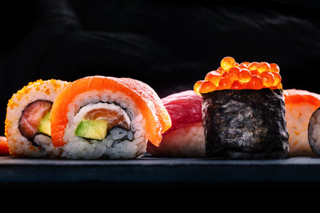 Sushi rolls on a black background. Uramaki with salmon, avocado, and cream cheese, and ikura maki rollの写真素材