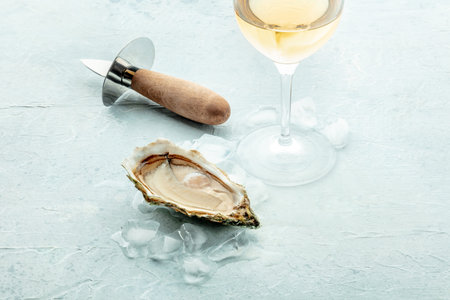 Fresh raw oyster with a glass of wine and an oyster knife, on ice, on a slate background