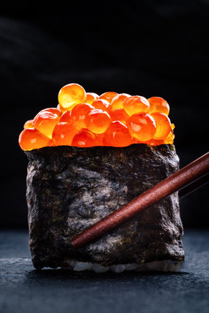 Ikura sushi maki roll with chopsticks on a black background, with a place for textの写真素材