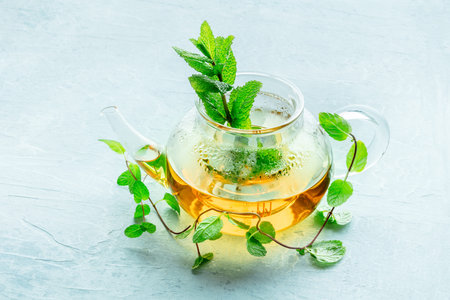 Mint tea. A tea pot with fresh peppermint leaves steeping in hot water, on a blue background