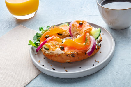 Lox bagel. A breakfast of a sandwich with smoked salmon and fresh vegetables on a plate, with orange juice and coffeeの写真素材
