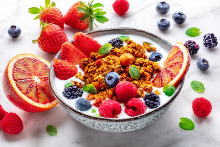 Granola with yogurt and fresh fruit. Organic gourmet muesli on a marble table with ingredients. Strawberry, orange, and mintの写真素材