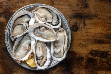 Fresh raw oysters on ice, overhead flat lay shot on a rustic wooden table, with lemon, with copy spaceの写真素材