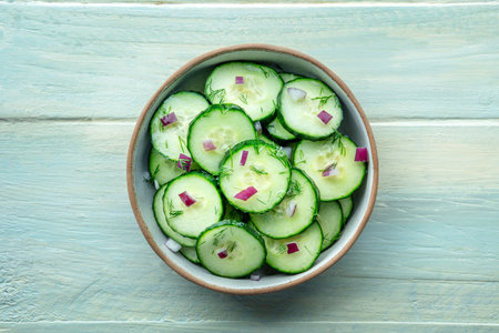 Cucumber salad with dill and red onion, overhead flat lay shot on a rustic wooden table in a bowlの写真素材