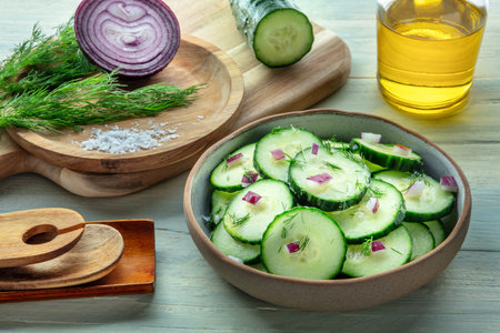 Cucumber salad with olive oil, dill, and red onion, on a rustic wooden table in a kitchen, healthy organic cookingの写真素材