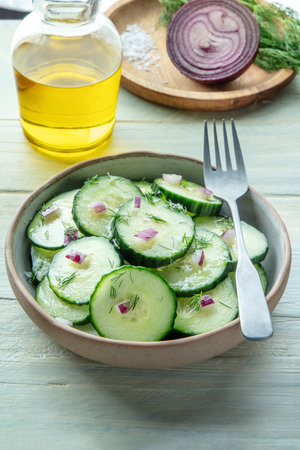 Cucumber salad with olive oil, dill and red onion, on a rustic wooden table with ingredients, cooking in the kitchenの写真素材