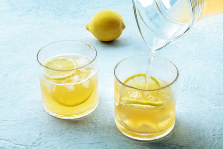 Lemonade poured from a jug into a glass, with a fresh lemon, on a blue slate backgroundの写真素材