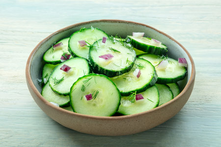 Cucumber salad with dill and red onion, on a rustic wooden table in a bowl, healthy organic vegetable dietの写真素材