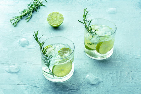 Gin tonic, two glasses of gin with soda, lime, rosemary, and plenty of ice, on a blue background, fresh summer cocktailsの写真素材