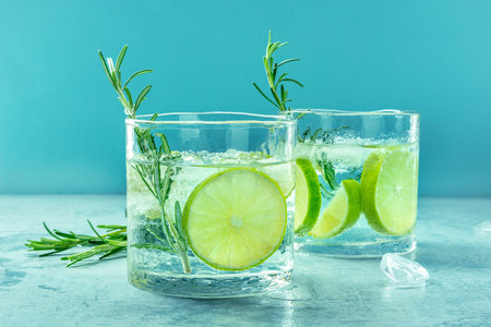 Gin tonic glasses, side view with rosemary and lime. Fresh summer cocktail with ice on a blue backgroundの写真素材