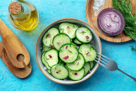 Cucumber salad with olive oil, dill, and red onion, on a blue background, healthy organic vegetable dish, overhead flat lay shot with ingredientsの写真素材