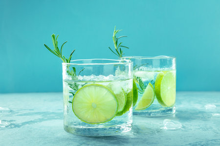 Gin tonic, two glasses of gin with soda, lime, rosemary, and plenty of ice, side view on a blue background, fresh summer cocktailsの写真素材