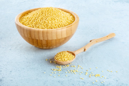 Millet, ancient African grain, in a wooden bowl on a blue background, with a spoon. Healthy vegan side dishの写真素材