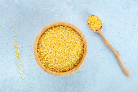 Millet, ancient African grain, in a wooden bowl on a blue background, with a spoon, overhead flat lay shot. Healthy vegan side dishの写真素材