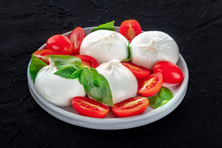Buffalo Mozzarella, fresh cherry tomatoes, and basil leaves, Italian Caprese salad on a black backgroundの写真素材