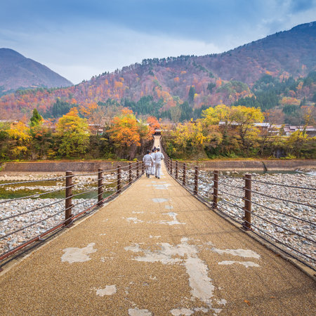 SHIRAKAWA GO, JAPAN - NOV. 12, 2014 : Unidentified people cross the bridge over Shogawa river to the Ogimachi Village, one of Japan's UNESCO world heritage sites in Shirakawa Go, Japan.のeditorial素材