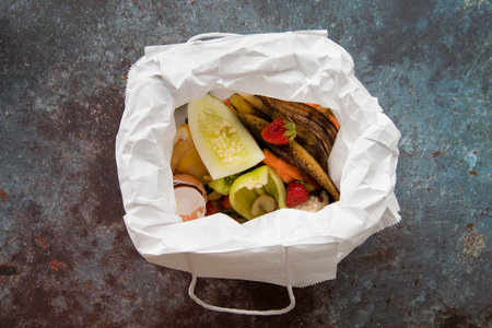 Top view of a white paper bag filled with food waste on a table.