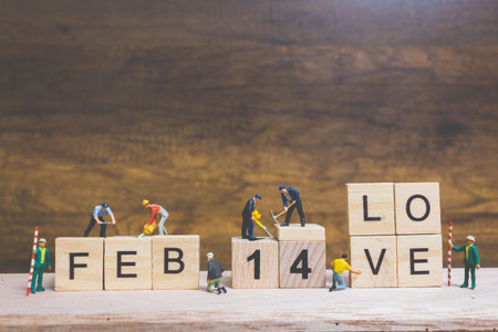 Miniature people : Worker team building word  14 FEB  on wooden block with wooden background , Valentine's day concept