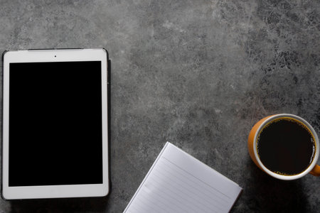 Coffee break. Top view yellow cup of coffee with tablet and Note paper on a table background