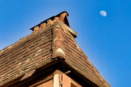 Old roof on a dormer window of a 200 year old French farmhouse in a state of disrepair with loose, broken and missing tiles. Moon in the background.の写真素材