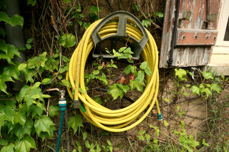 Yellow and green hosepipes on a reel and connected to a tap fixed to a French farmhouse wall next to shabby shuttersの写真素材